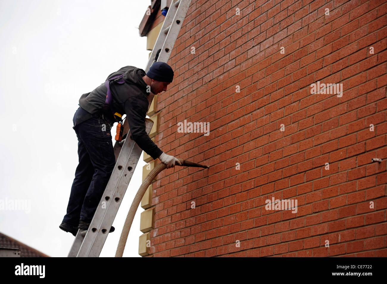 Raumwandisolierung. Ein Arbeiter bläst Isoliermaterial in Hohlwand von Wohn-Immobilien Haus energieeffizient Stockfoto