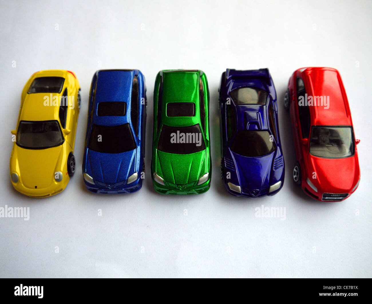 5 Spielzeug-Autos hintereinander.  Gelb blau grün lila und rot. Stockfoto