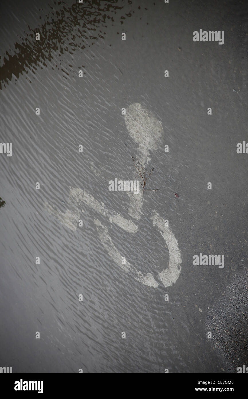 Bemaltes Parkschild für Menschen mit Behinderung auf Asphalt, der an einem regnerischen Tag mit Wasser bedeckt ist Stockfoto