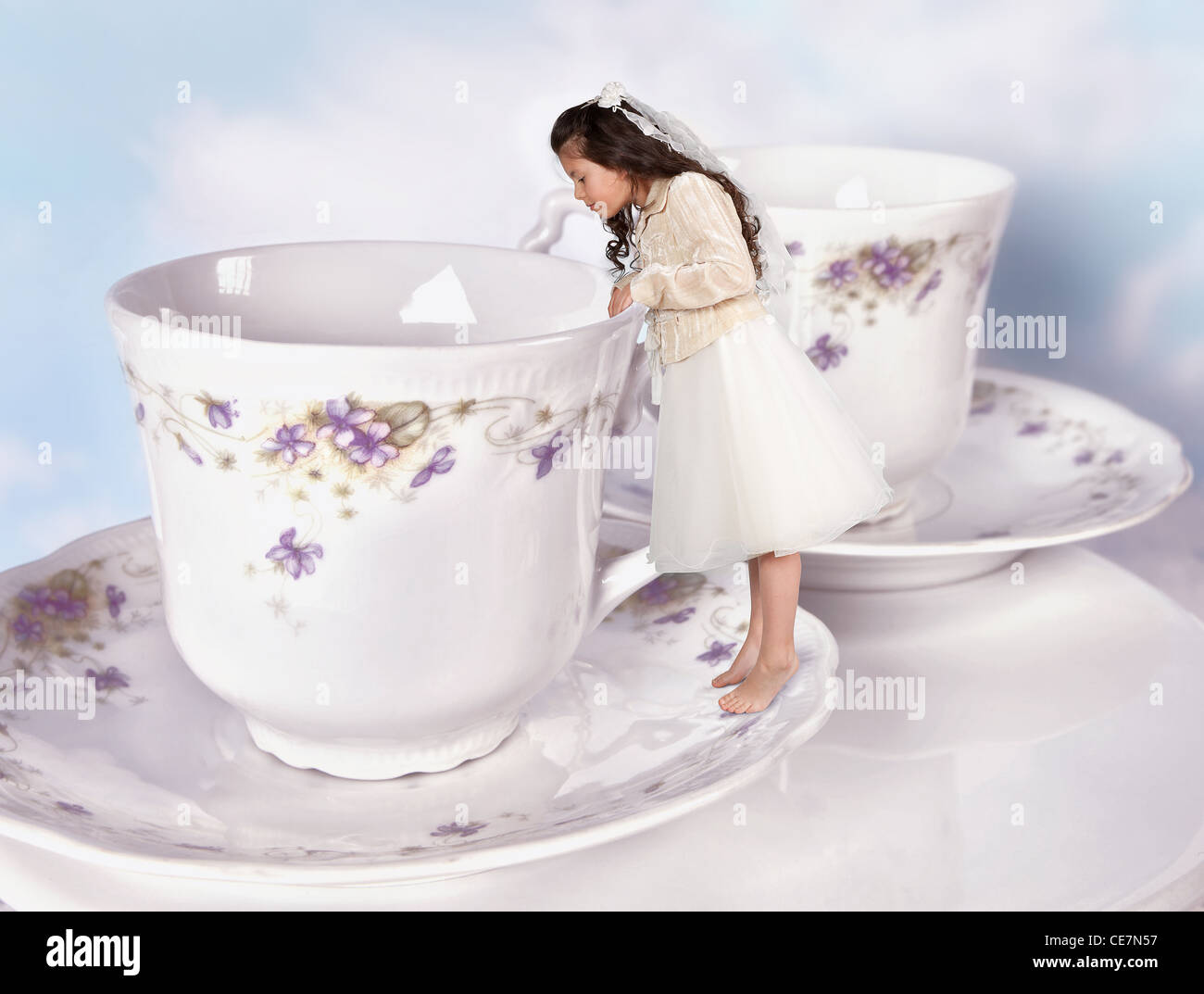 Miniatur-Mädchen in Alice im Wunderland Kleid geschrumpft auf die Größe einer Teetasse Stockfoto