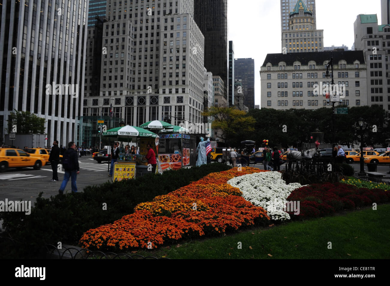 Graues Hochhaus Himmelsblick, orange weiße Blumen, Menschen, Autos, Bürgersteig Eis Ständen, Grand Army Plaza, 5th Avenue, New York Stockfoto