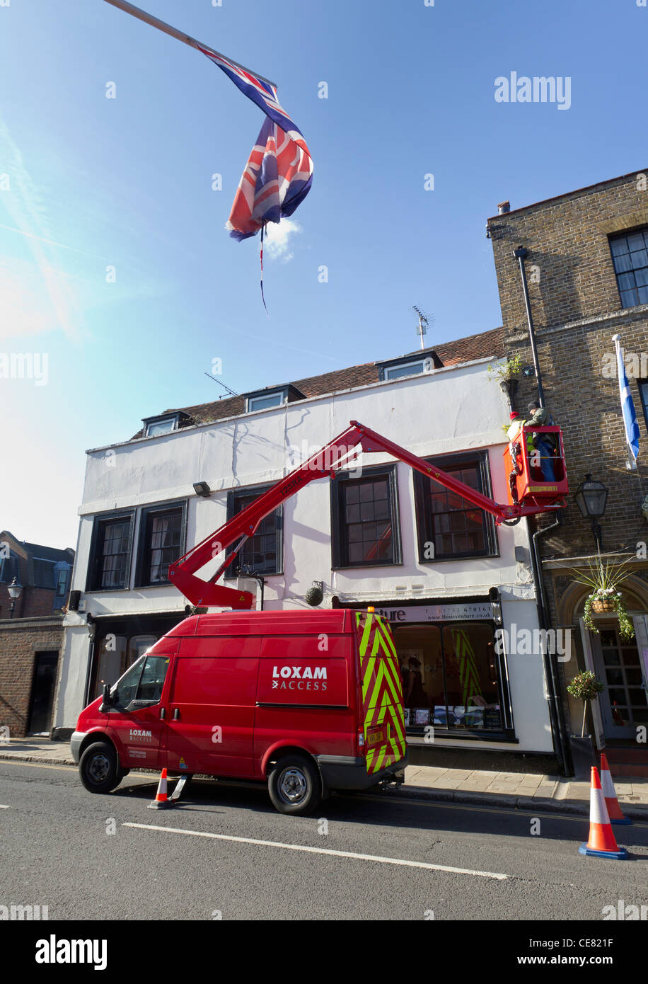 Arbeiter in einer Hubarbeitsbühne (Arbeitsbühne) und ein Union Jack-Flagge über ihnen im Vordergrund. Stockfoto