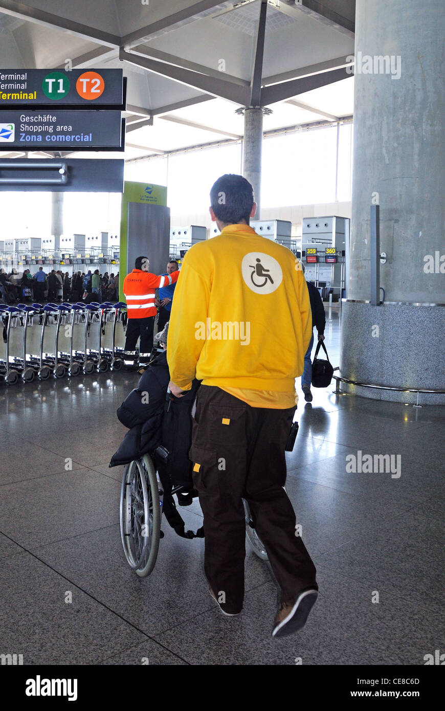 Porter drängen Passagier im Rollstuhl in Richtung Check-in-Schaltern im Terminal 3, Flughafen Malaga, Malaga, Spanien, Europa. Stockfoto