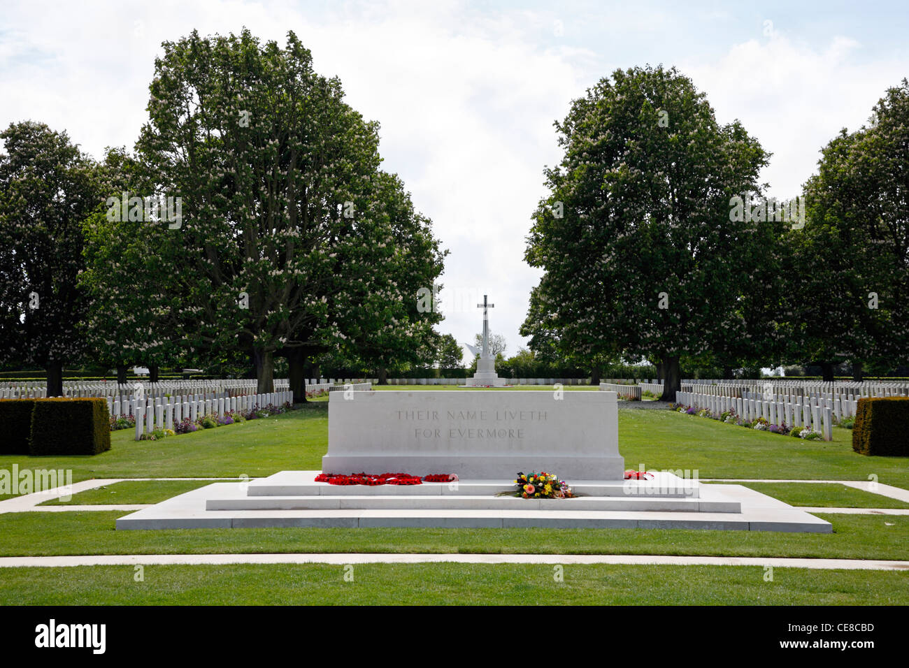 Denkmal mit Blumen und das Kreuz des Opfers in der Ferne am britischen Soldatenfriedhof Bayeux Bayeux, Normandie, Frankreich. Soldatenfriedhof. Stockfoto