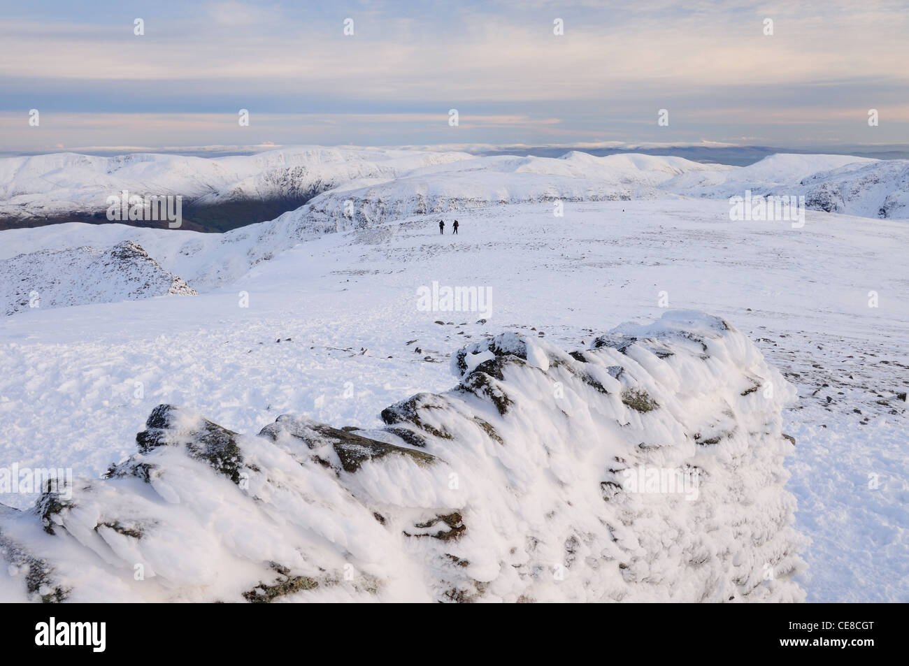 Käserand Schneewand des Tierheims Gipfel auf Lakelandpoeten mit zwei Wanderern in Richtung Striding Edge im Hintergrund Stockfoto