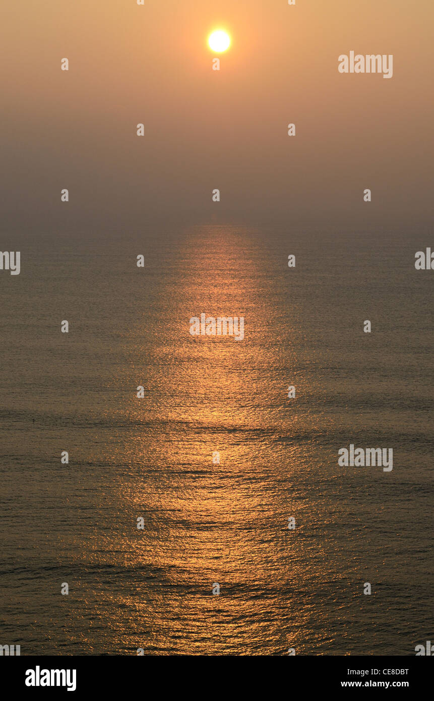 Trübe Sonnenuntergang am Perranporth, Cornwall, wirft eine Lichtspur über eine ruhige See Stockfoto