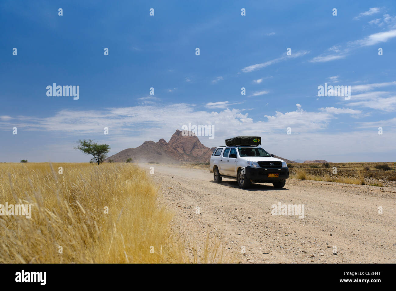 4 x 4 Fahrzeug auf der Schotterstraße aus dem fernen Gipfel der Spitzkoppe vorbei. Damaraland, Namibia. Stockfoto