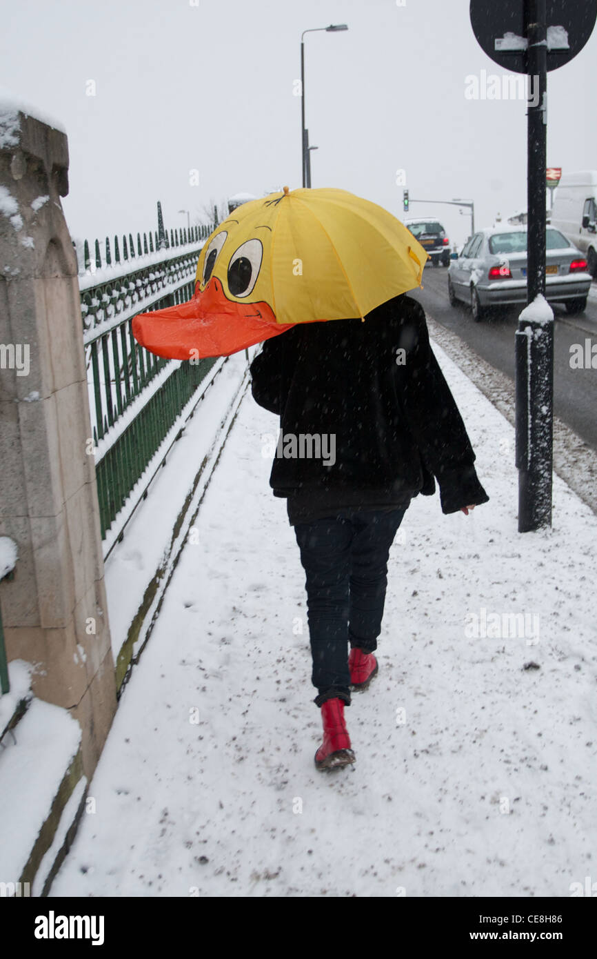 Eine Frau überquert eine Brücke im Schnee mit einem hellen farbigen Ente Schirm schützt ihr aus dem Schnee Stockfoto