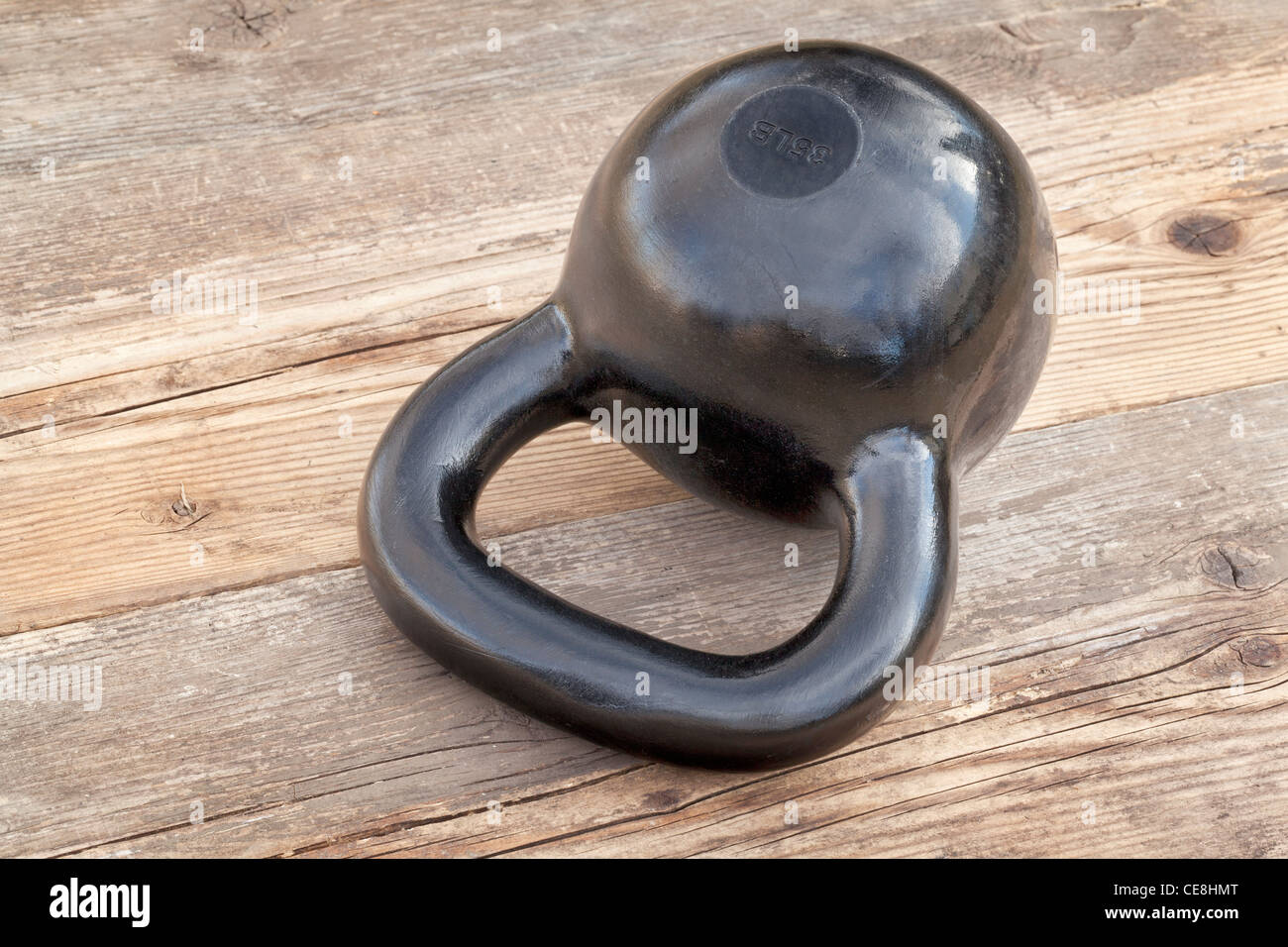 schwarze 35 lb Kettlebell für Krafttraining auf Holz Grunge Deck im Freien mit Himmel Reflexionen Stockfoto