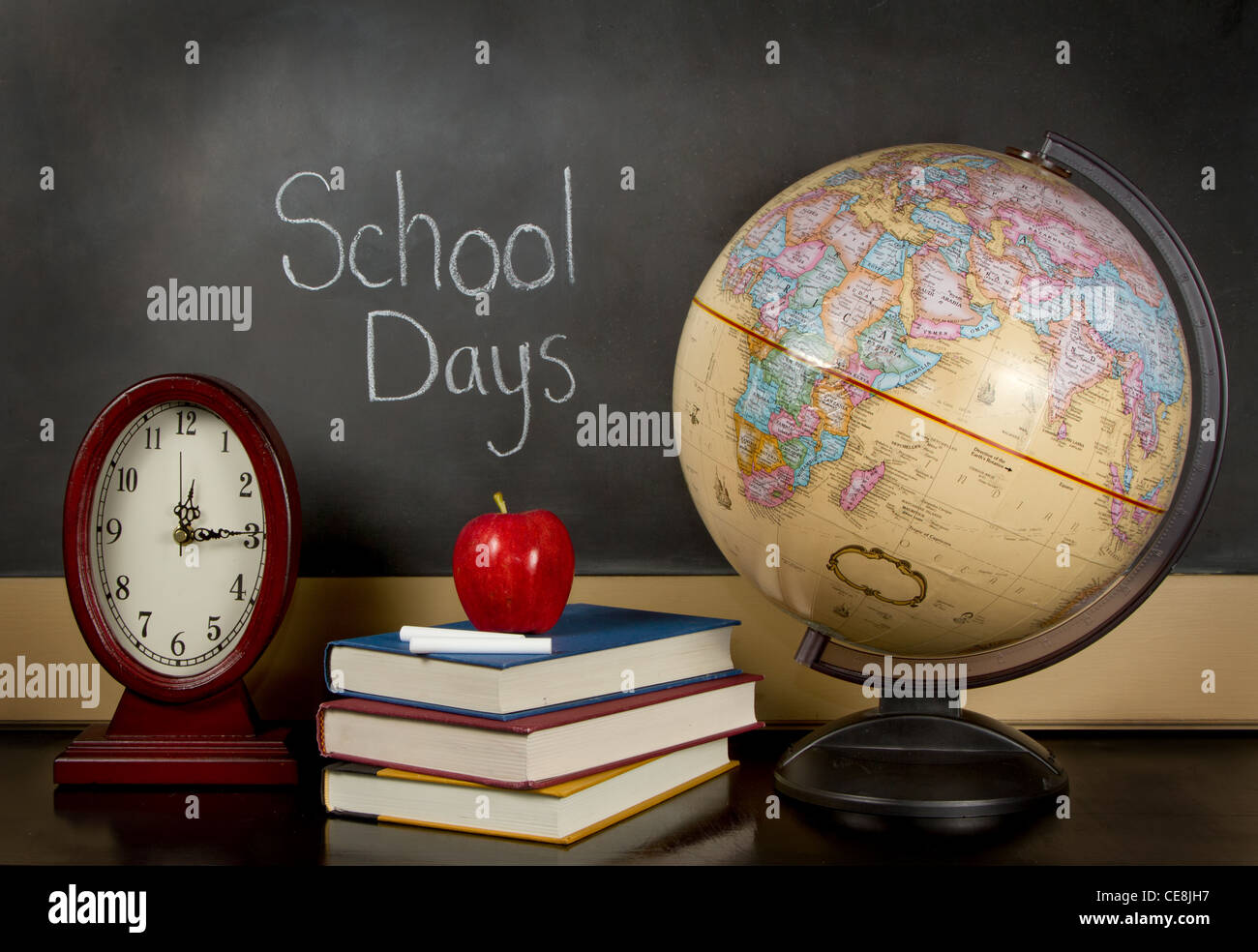 eine Tafel mit den Worten Schule Tagen geschrieben, eine Uhr, Bücher, Apfel, Kreide und eine Kugel auf einem Lehrer Schreibtisch sitzen. Stockfoto