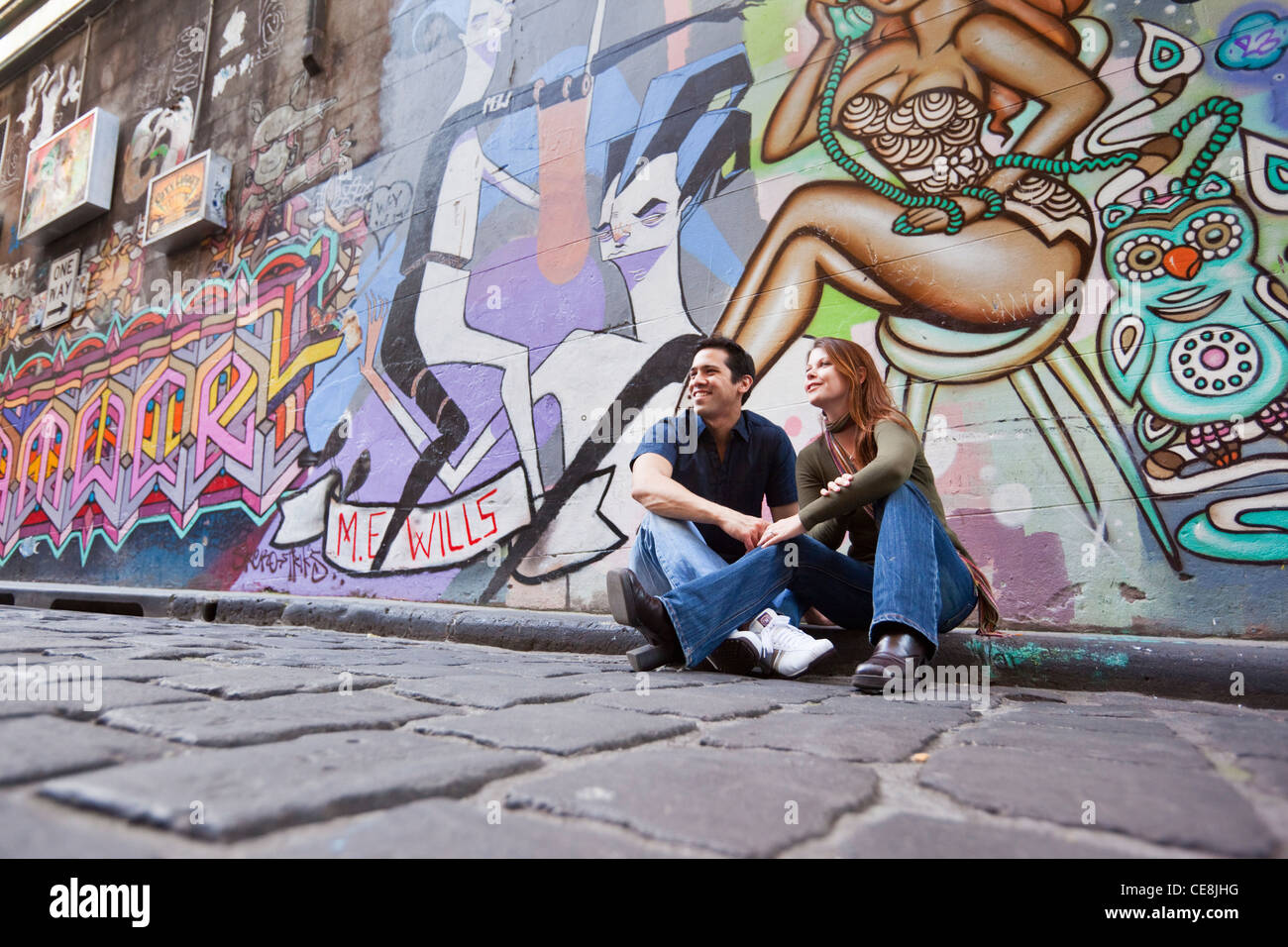 Paar sitzt in Stadt Gasse umgeben von urban street-Art. Hosier Lane, Melbourne, Victoria, Australien Stockfoto