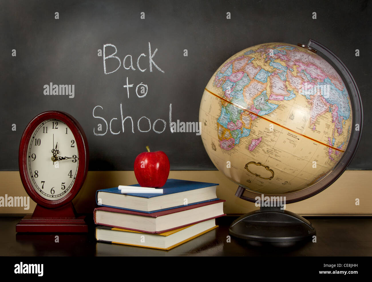eine Tafel mit den Worten zurück in der Schule geschrieben, eine Uhr, Bücher, Apfel, Kreide und eine Kugel auf einem Lehrer Schreibtisch sitzen. Stockfoto