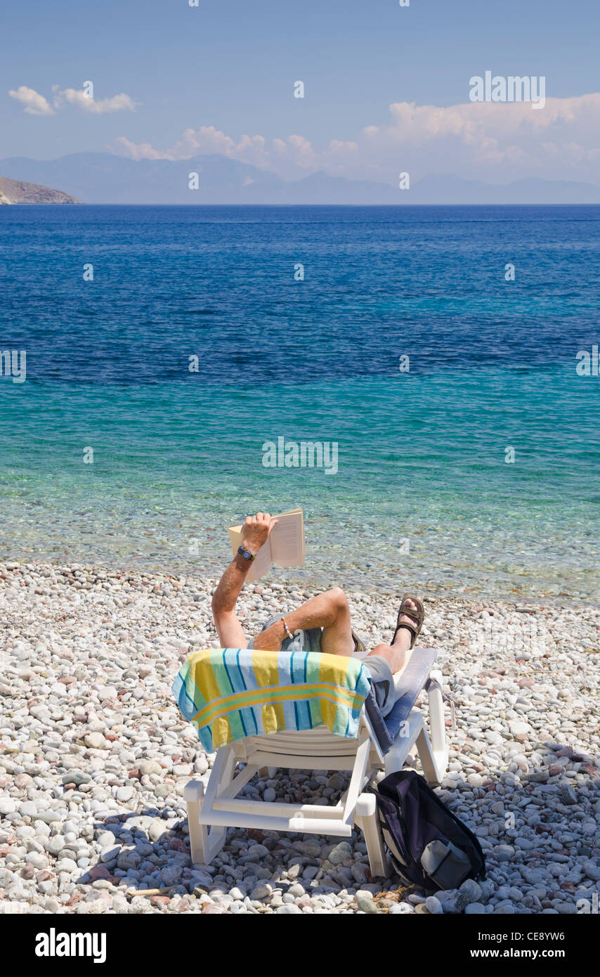 Mann liest ein Buch auf einem Liegestuhl Strand auf der Insel Tilos Griechenland Stockfoto