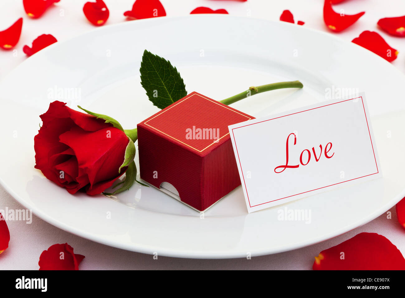 Foto von einer roten Rose auf einem Teller mit einer Kiste für einen Verlobungsring und eine Karte mit dem Wort Liebe Stockfoto