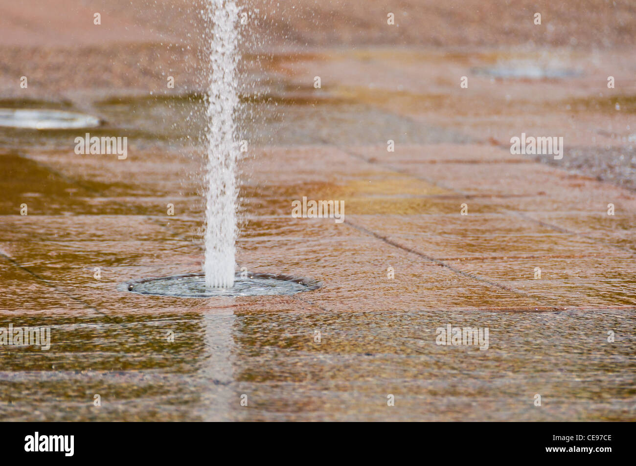 Ein Brunnen Wasserstrahl Besprühen mit Wasser bis auf eine gemusterte Boden Stockfoto