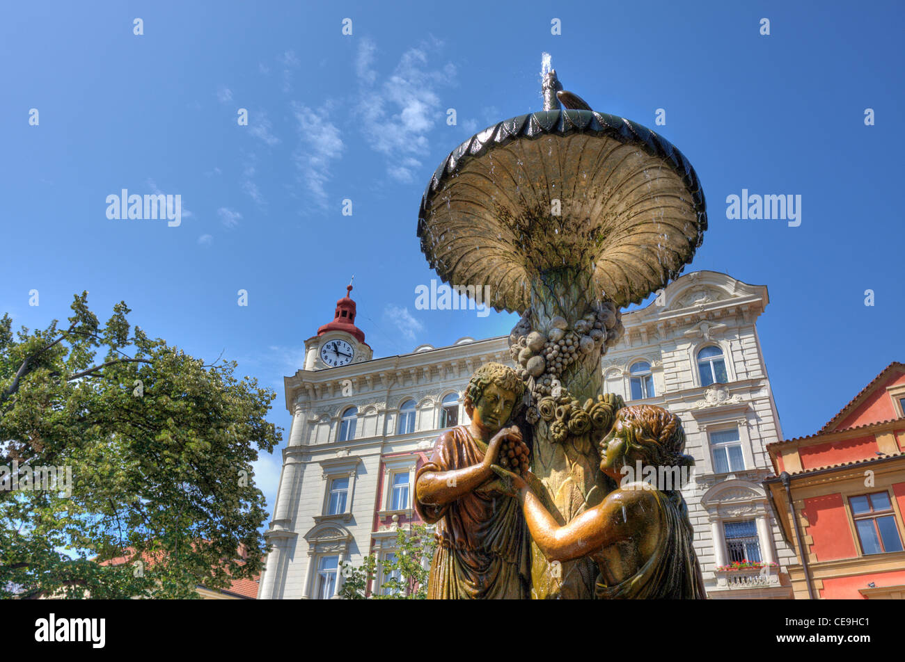 Alter Brunnen mit Skulpturen vor weißes Gebäude mit Uhr in Prag, Tschechien. Stockfoto