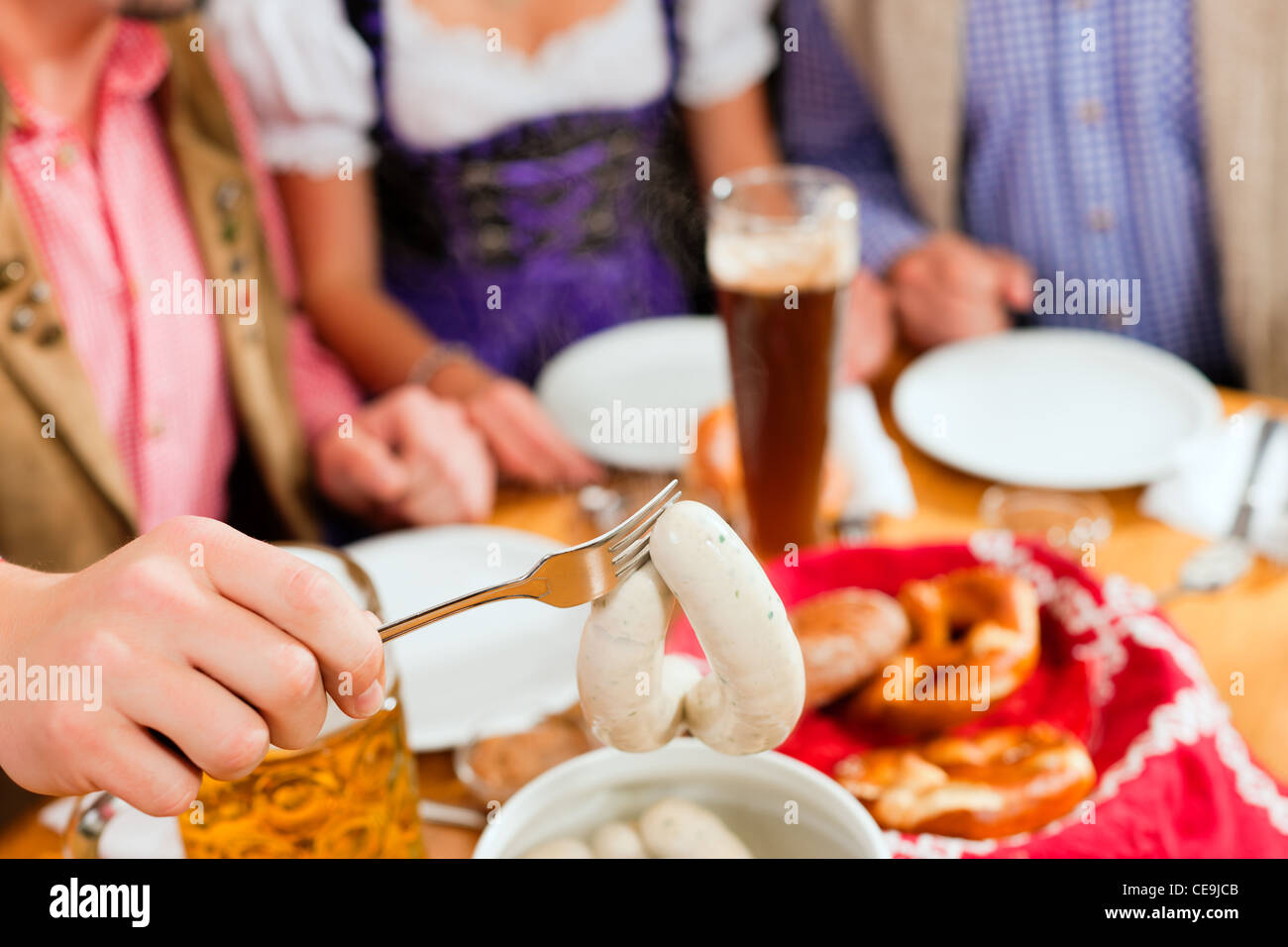 Gruppe von jungen Männern und Frauen in traditionellen bayerischen Tracht mit einem Frühstück mit weißen Weißwurst, Brezel und Bier Stockfoto