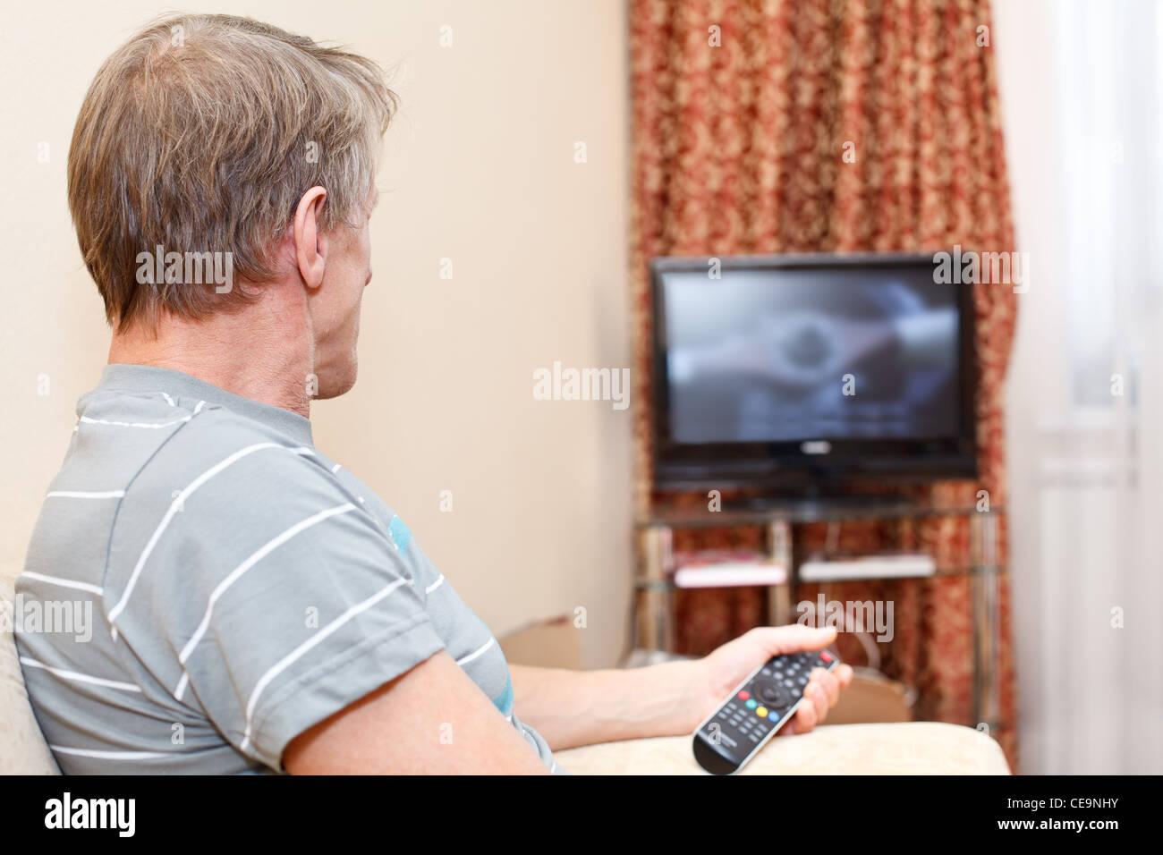 Ältere Mann mit Fernbedienung auf Couch sitzen und TV-Gerät betrachten Stockfoto