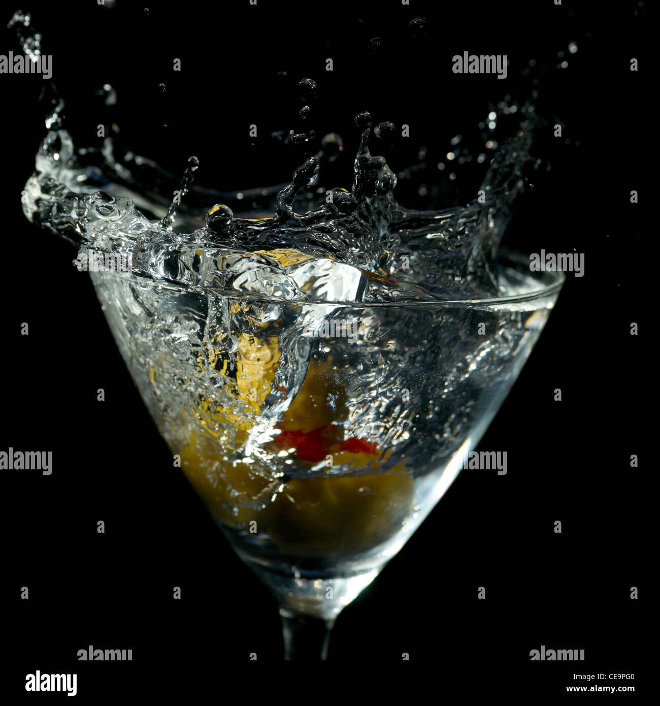 Wasser oder andere klare Flüssigkeit spritzt aus einem Martini-Glas auf schwarzem Hintergrund. Stockfoto