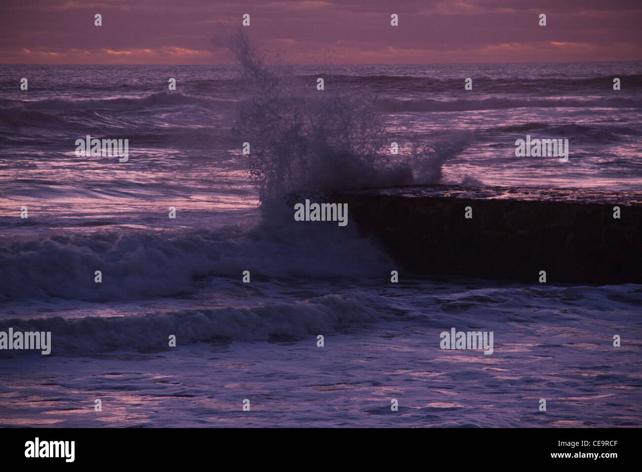 Eine Welle auf einen Steg abstürzt, nachdem die Sonne untergegangen ist. Carcavelos Strand, größere Lissabon, Portugal. Stockfoto