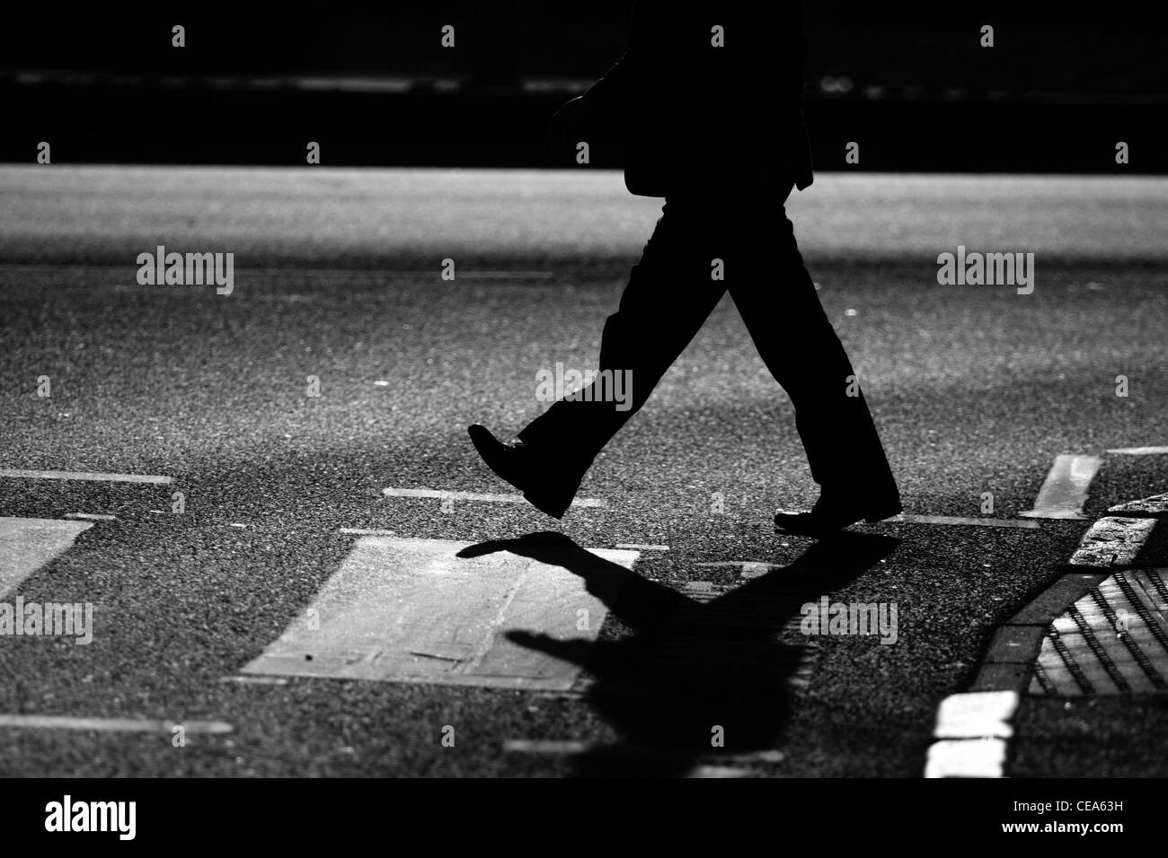 Die Beine eines Mannes als er eine Straße auf einem Zebrastreifen in London überquert Stockfoto