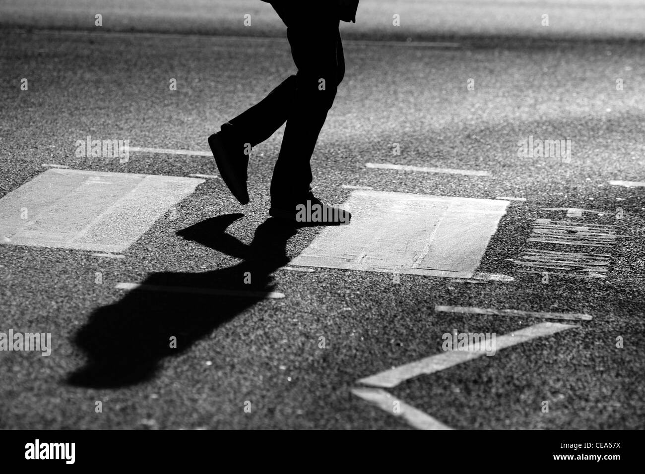 Die Beine eines Mannes als er eine Straße auf einem Zebrastreifen in London überquert Stockfoto