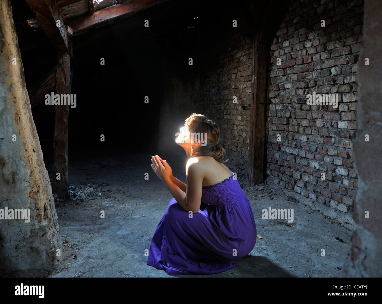 Junge Frau kniend im Dachboden beten Lichtschein auf ihrem Gesicht Stockfoto
