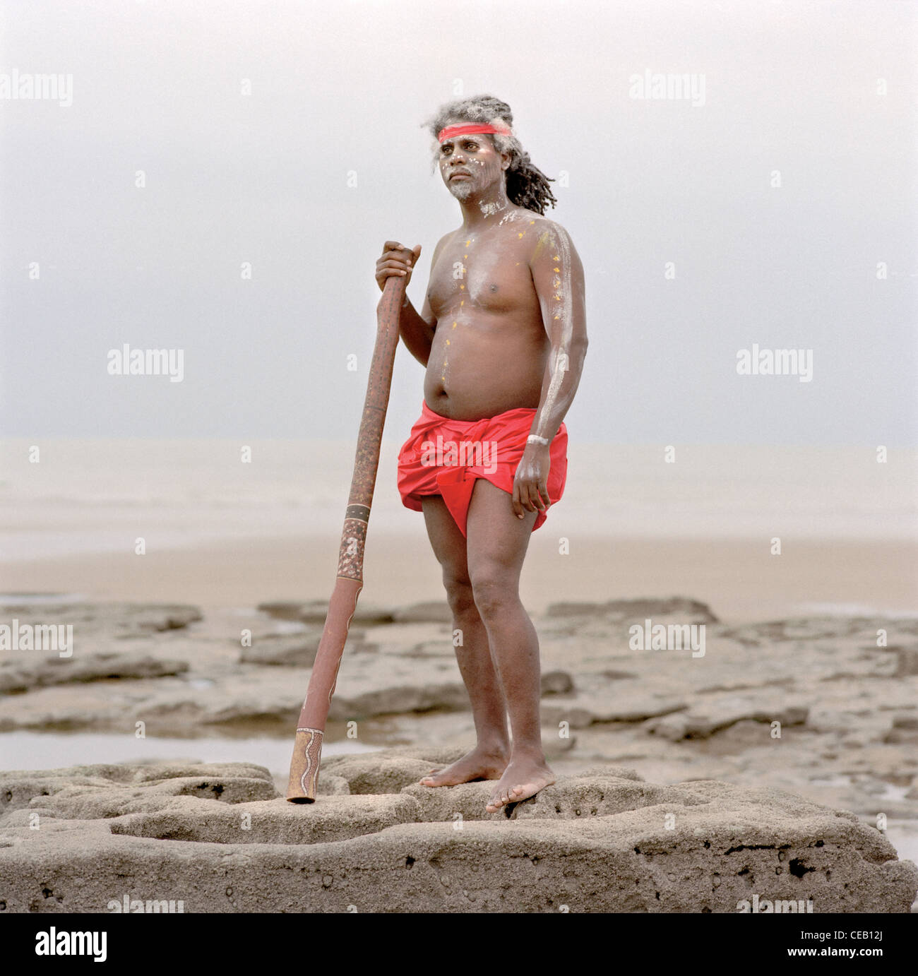 Aborigines Mann an einem Strand ein Didgeridoo zu spielen. Stockfoto