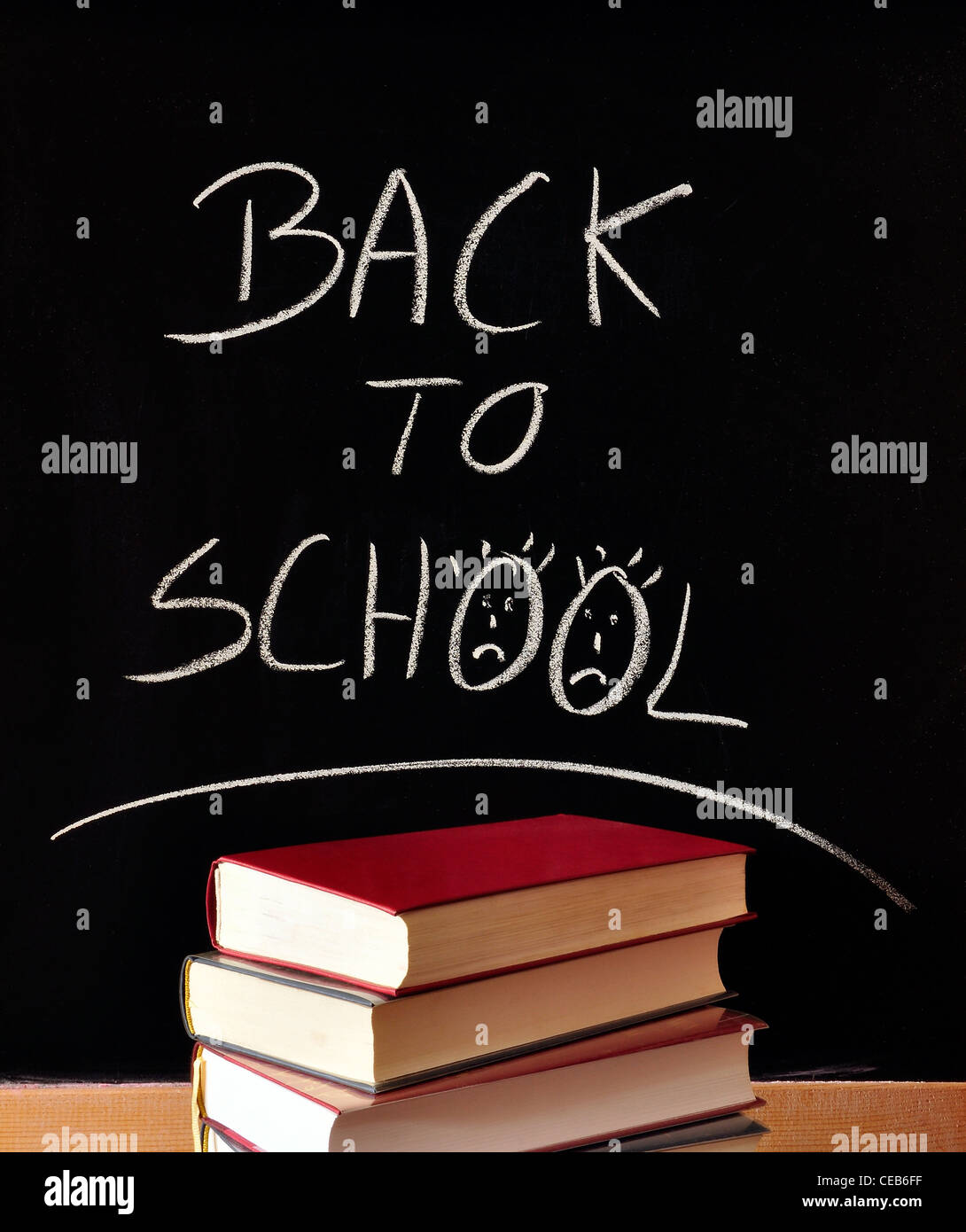 die Worte "Back to School" in Kreide auf eine Tafel, Bücher, traurige Smileys geschrieben Stockfoto