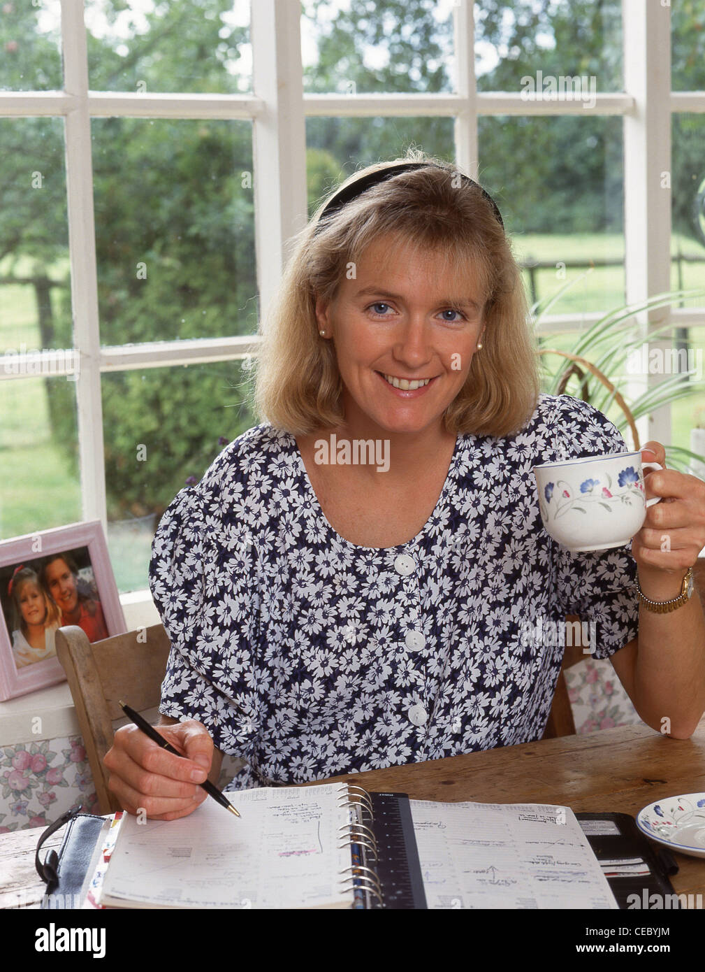 Junge Frau Tasse Tee trinken und Schreiben von Noten, Surrey, England, Vereinigtes Königreich Stockfoto
