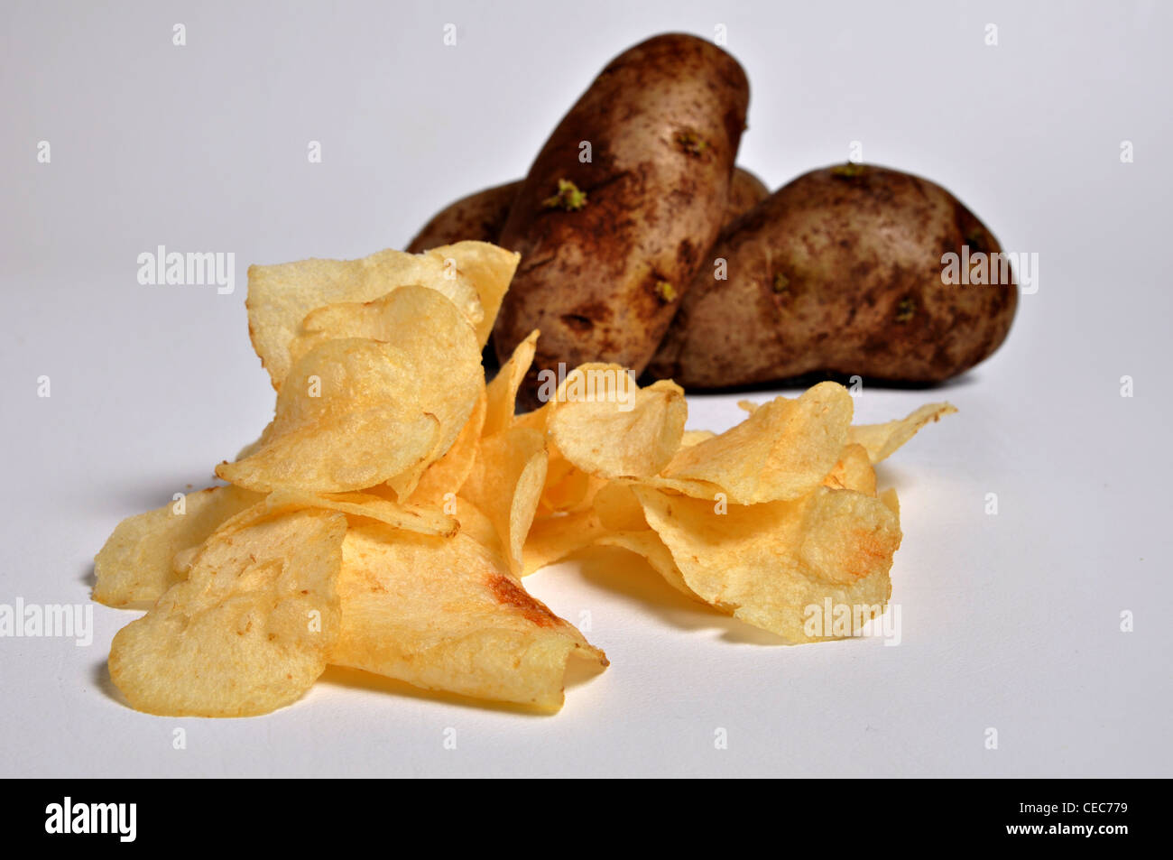 ein Haufen von Kartoffel-Chips sitzen auf einem weißen Hintergrund mit ein paar Kartoffeln im Hintergrund. Stockfoto