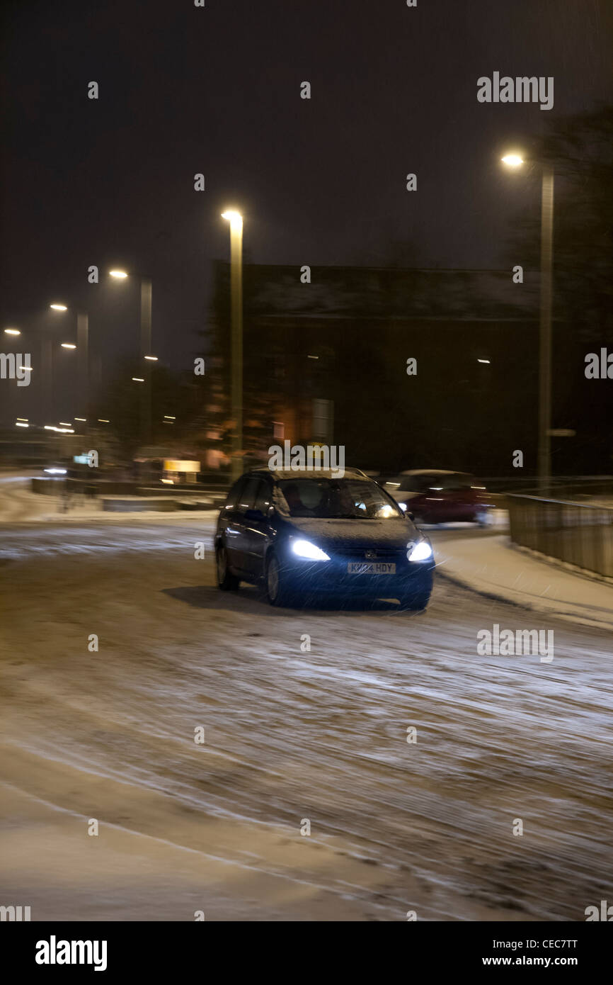 Auto mit Licht fahren um einen Kreisverkehr bei winterlichen/Schnee Wetter bei Nacht Stockfoto