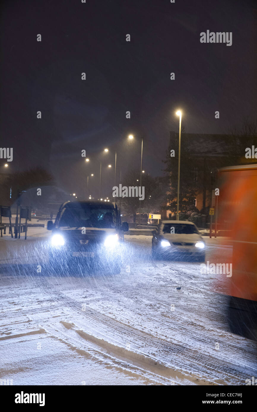 Autos mit Licht fahren um einen Kreisverkehr bei winterlichen/Schnee Wetter bei Nacht Stockfoto