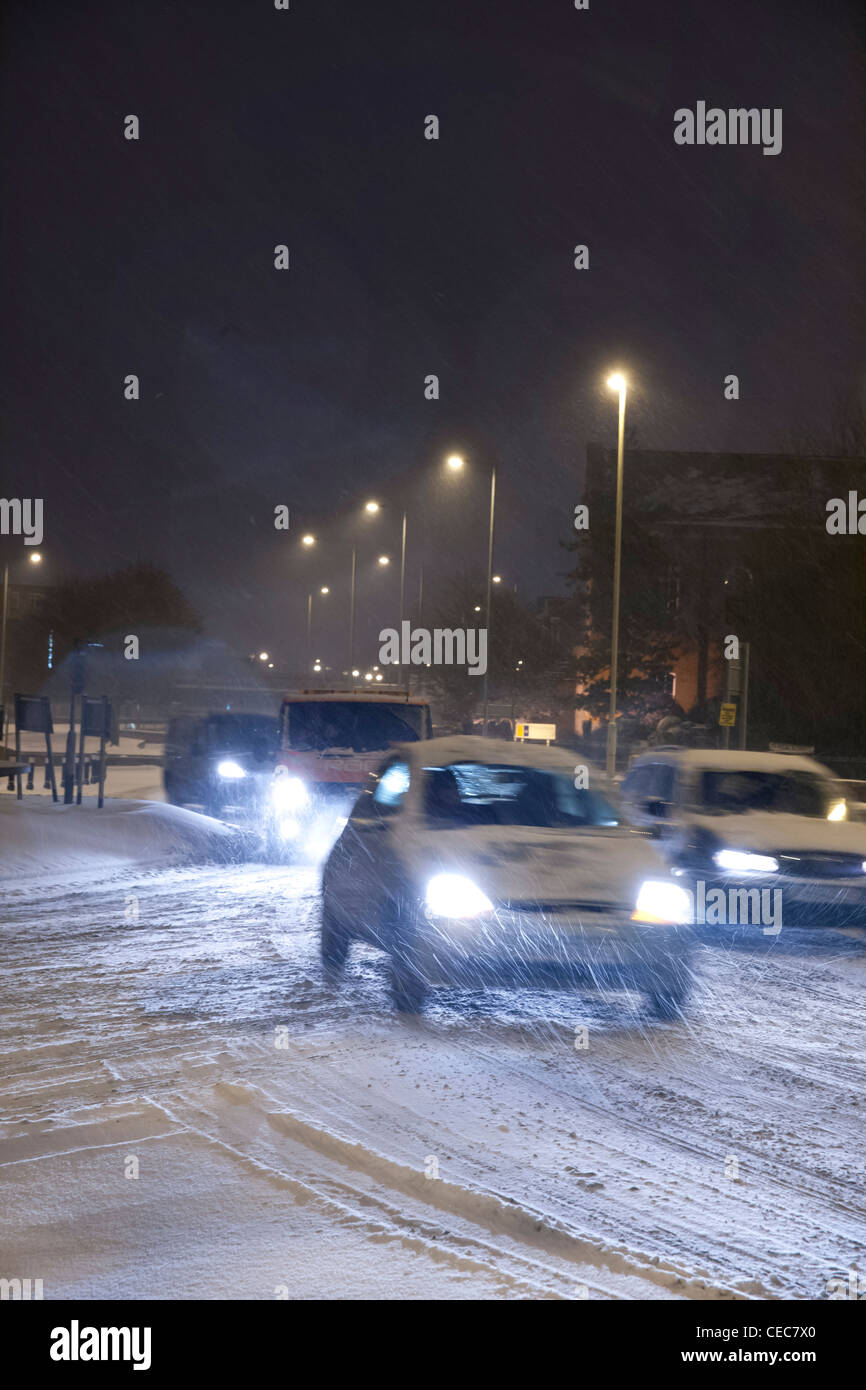 Autos und Lieferwagen mit Licht fahren um einen Kreisverkehr bei winterlichen/Schnee Wetter bei Nacht Stockfoto