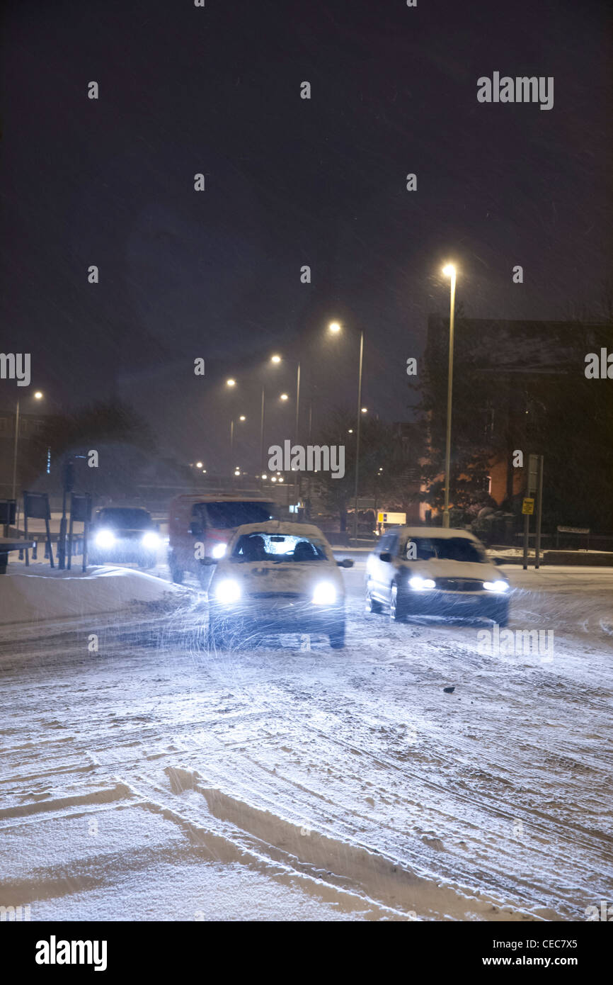 Autos mit Licht fahren um einen Kreisverkehr bei winterlichen/Schnee Wetter bei Nacht Stockfoto