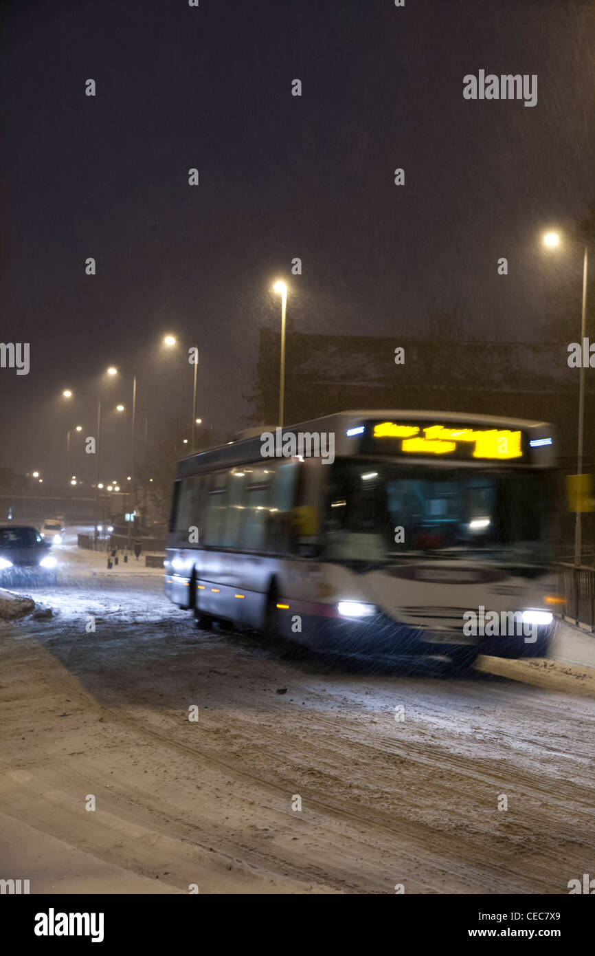 Bus mit Licht fahren um einen Kreisverkehr bei winterlichen/Schnee Wetter bei Nacht Stockfoto
