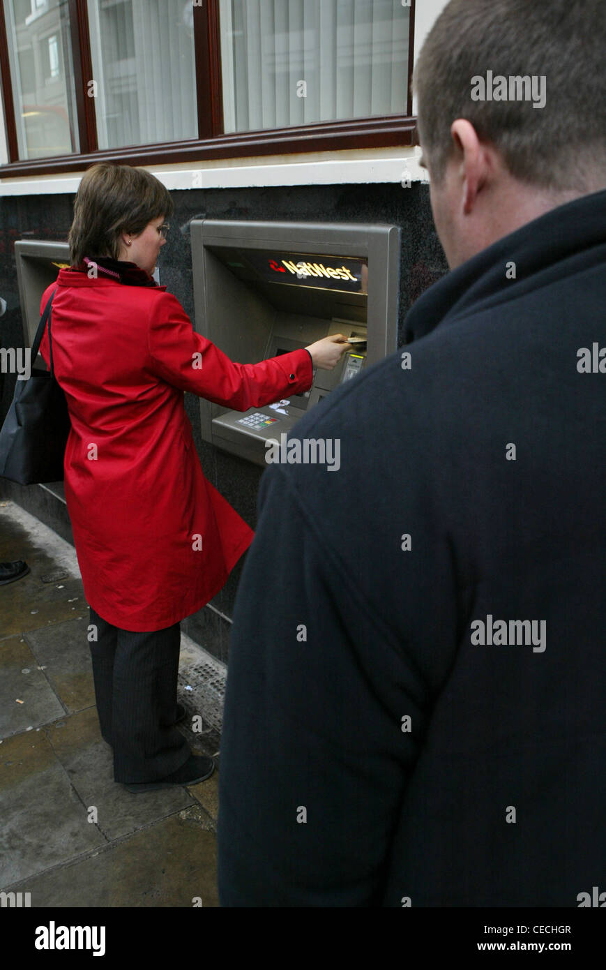 Frau Zeichnung Geld von einer Bank Bargeld Weichenantrieb von Verbrecher, der plant, sie bestehlen beobachtet Stockfoto