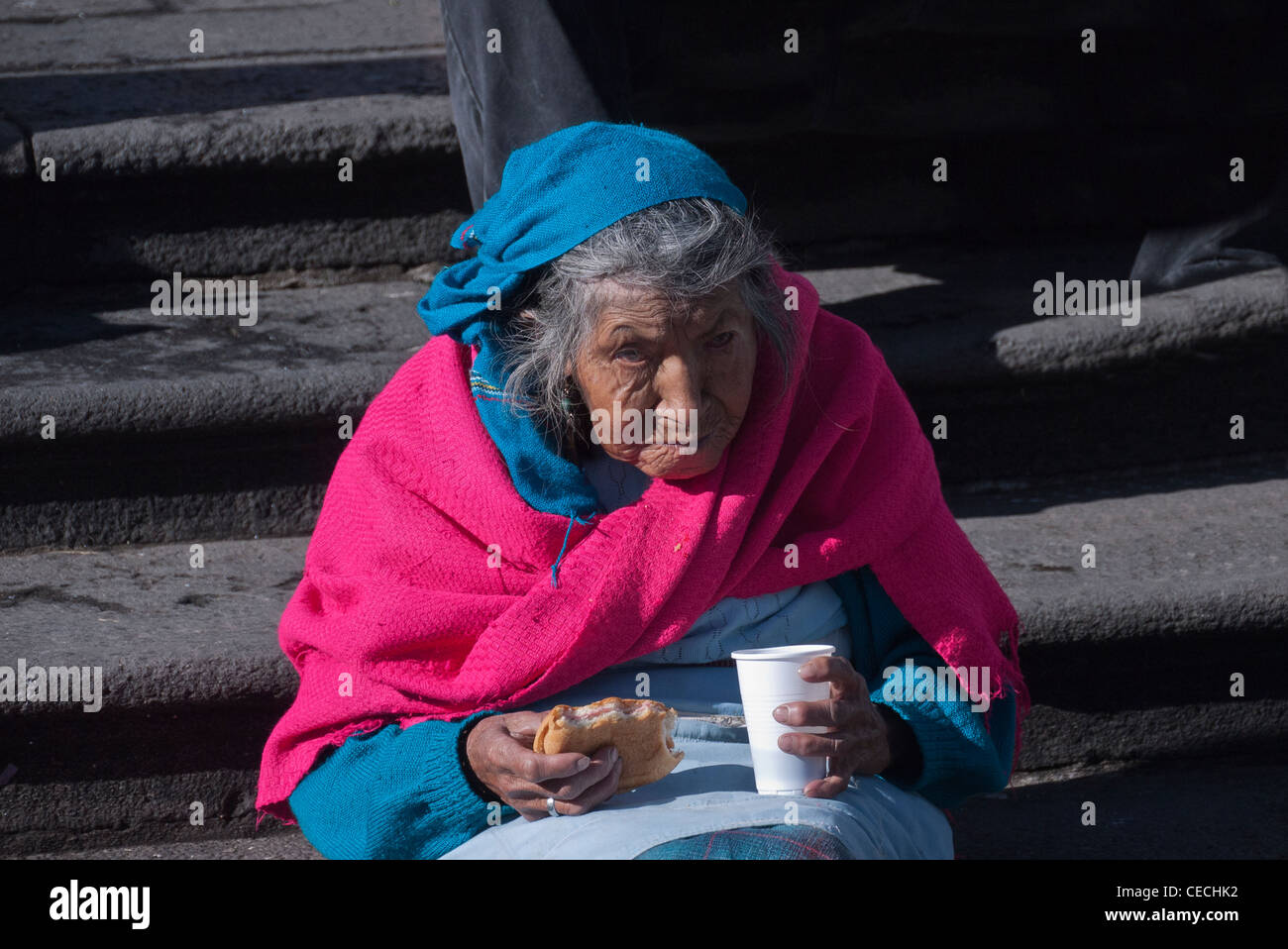 Eine 80-90 Jahre alt, sitzt ecuadorianische indigene Frau auf Schritte in San Francisco Plaza kostenlose Essen aus einer Gemeinschaftsküche. Stockfoto