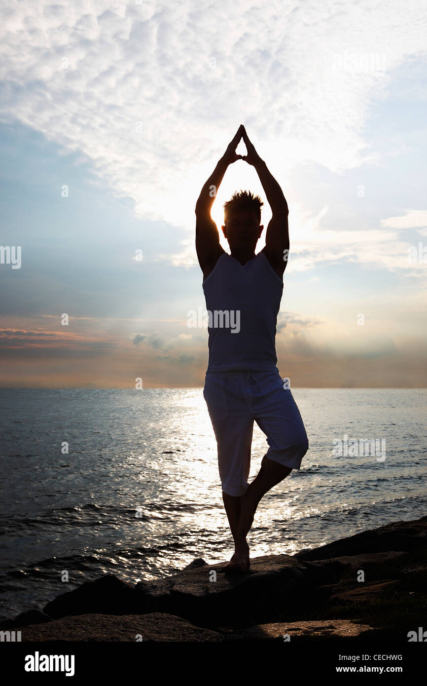 hinterleuchtete Bild der Mann tut Yoga neben Meer Stockfoto