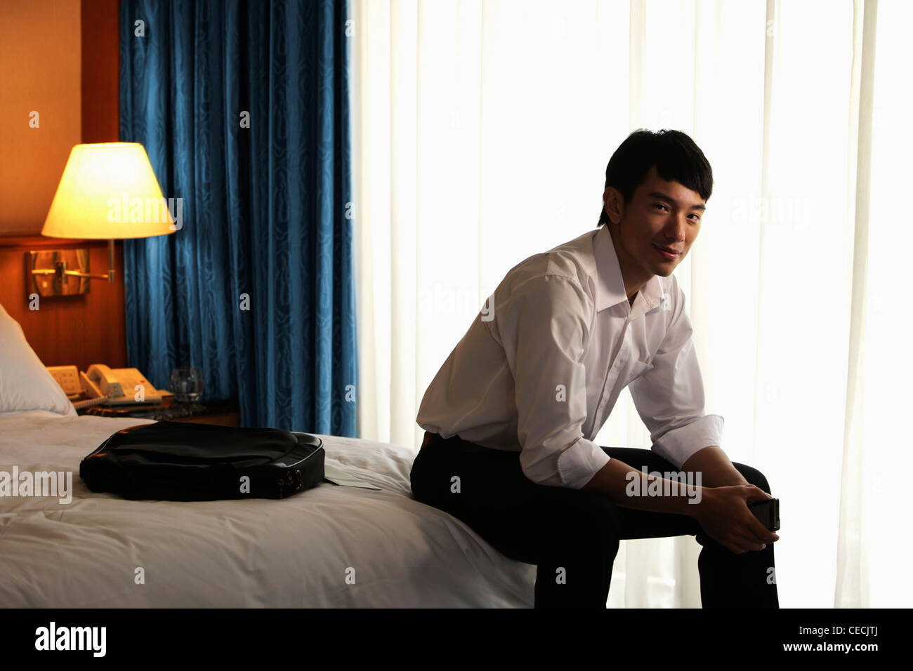 Junger Mann sitzt auf der Bettkante im Hotelzimmer Stockfoto