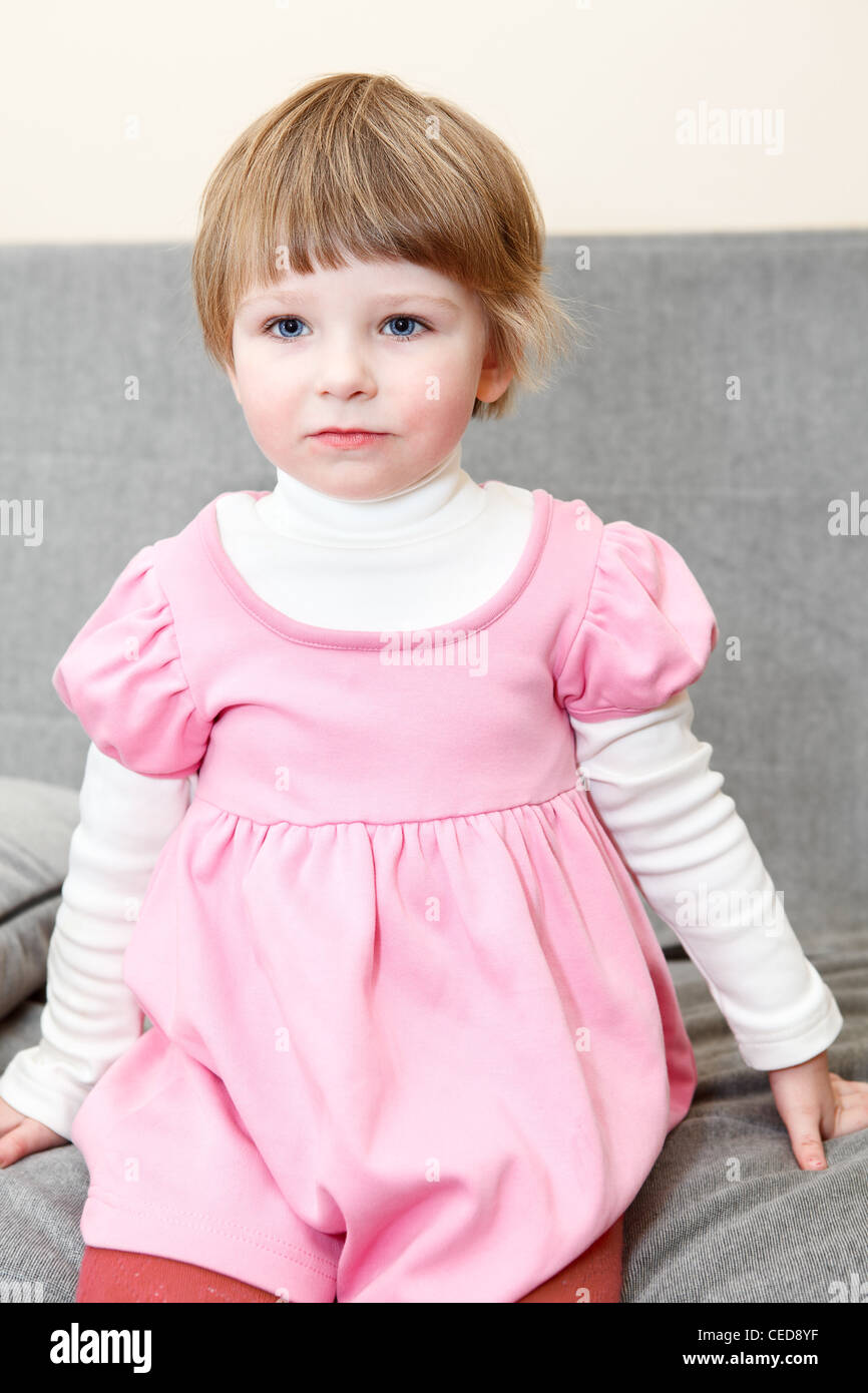 Porträt des kleinen Kaukasus russische Mädchen im rosa Kleid auf Couch sitzen und auf der Suche Stockfoto