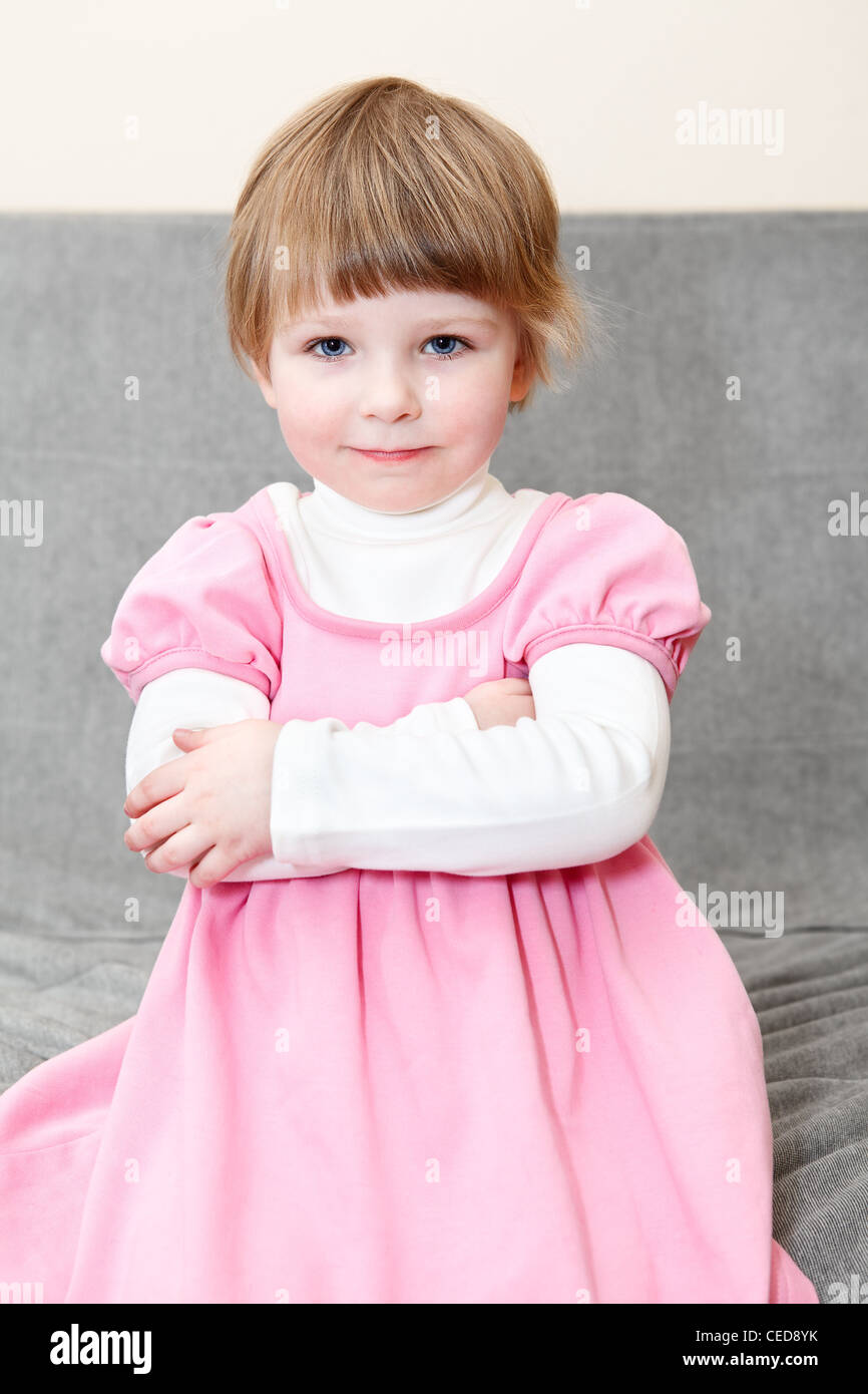 Porträt des kleinen Kaukasus russische Mädchen im rosa Kleid auf Couch sitzen und Blick in die Kamera Stockfoto