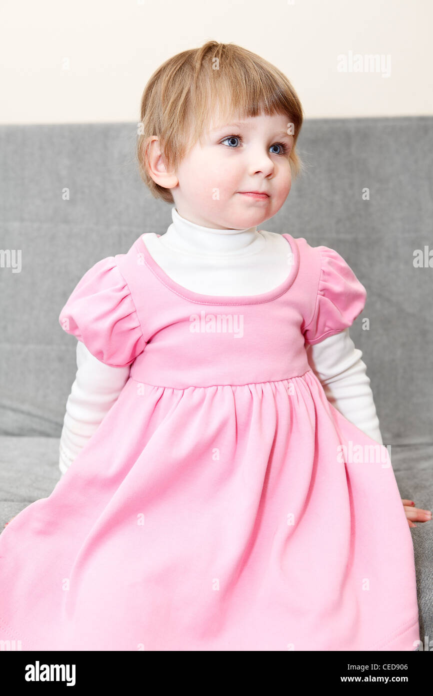 Porträt des kleinen Kaukasus russische Mädchen im rosa Kleid auf Couch sitzen und auf der Suche Stockfoto