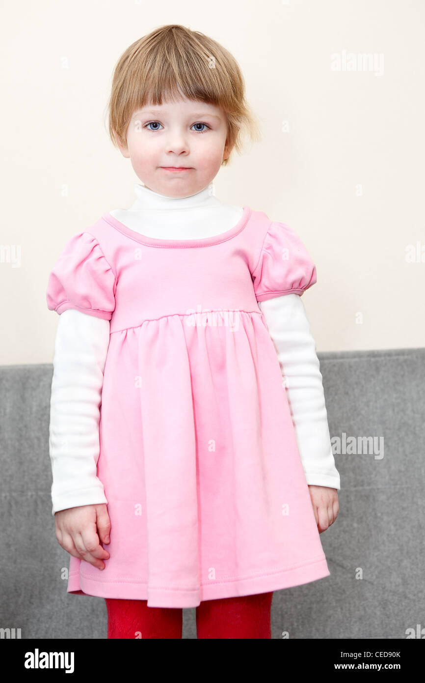 Porträt des kleinen Kaukasus russische Mädchen im rosa Kleid stehend auf Sofa und Blick in die Kamera Stockfoto