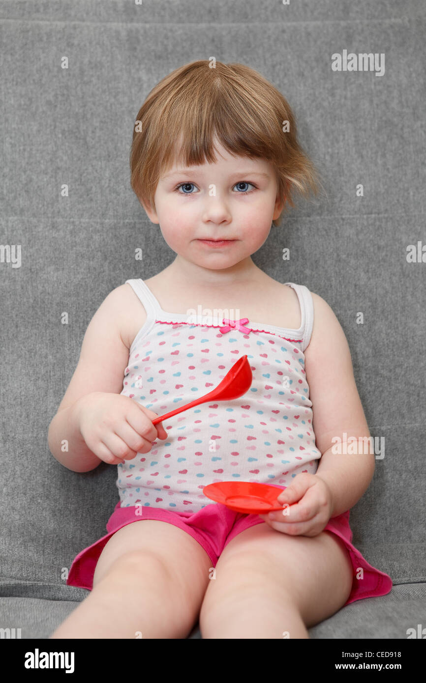 Porträt des kleinen kaukasischen Mädchen spielen auf Couch mit Löffel und Teller Spielzeug Stockfoto