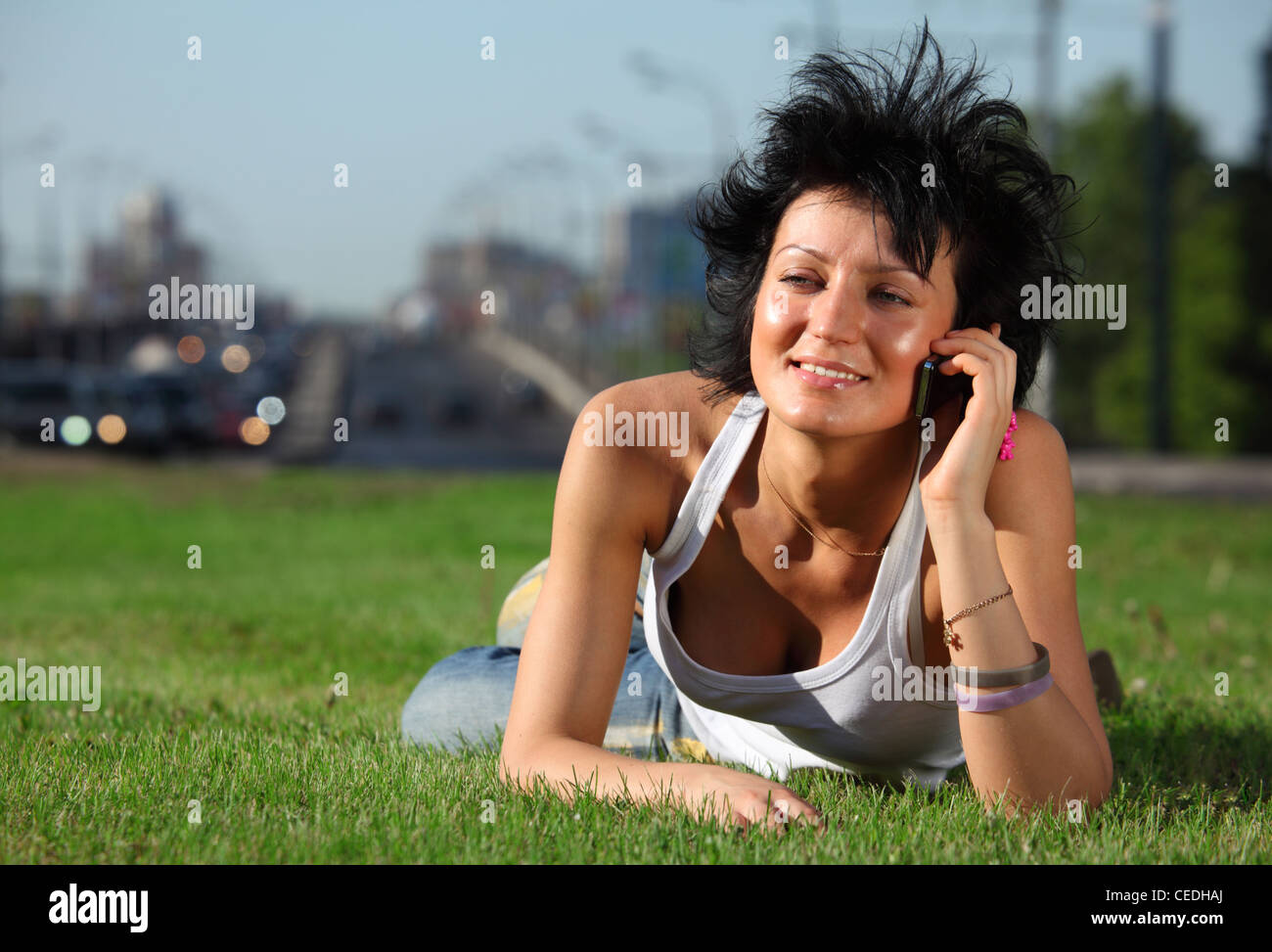 Mädchen liegt auf Rasen an Straße in Stadt und spricht per Telefon Stockfoto