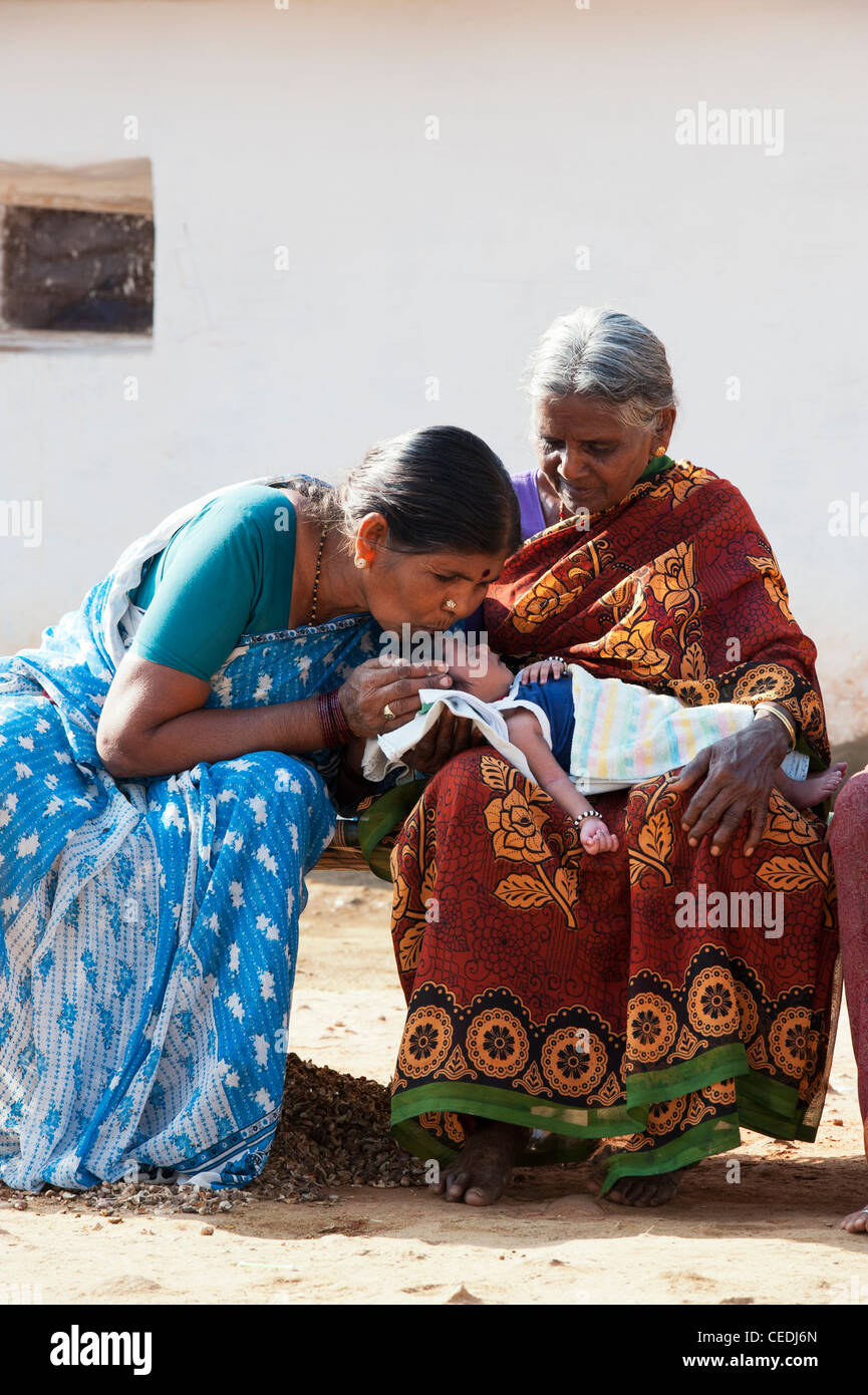 Indische Großmütter halten und küssen ein neugeborenes Baby in einem indischen Dorf. Andhra Pradesh, Indien Stockfoto