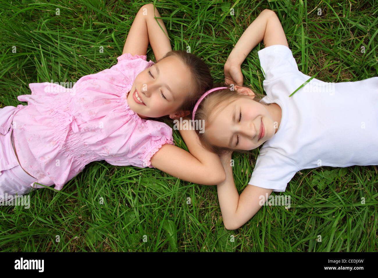 Zwei Mädchen liegen auf dem Rasen mit geschlossenen Augen, Kopf an Kopf Stockfoto