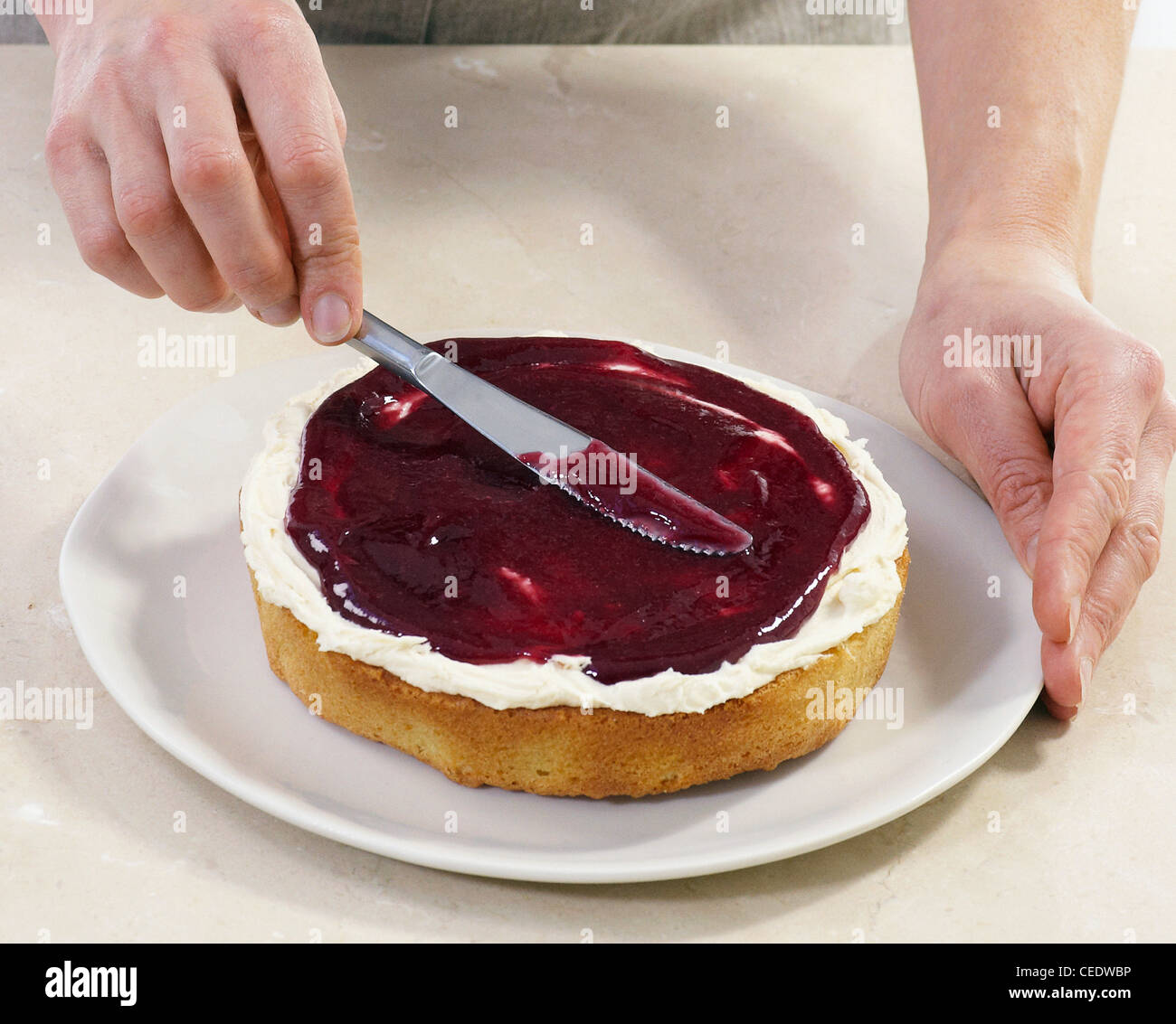 Verbreitung von Marmelade auf Buttercreme auf einer Victoria Biskuit Stockfoto