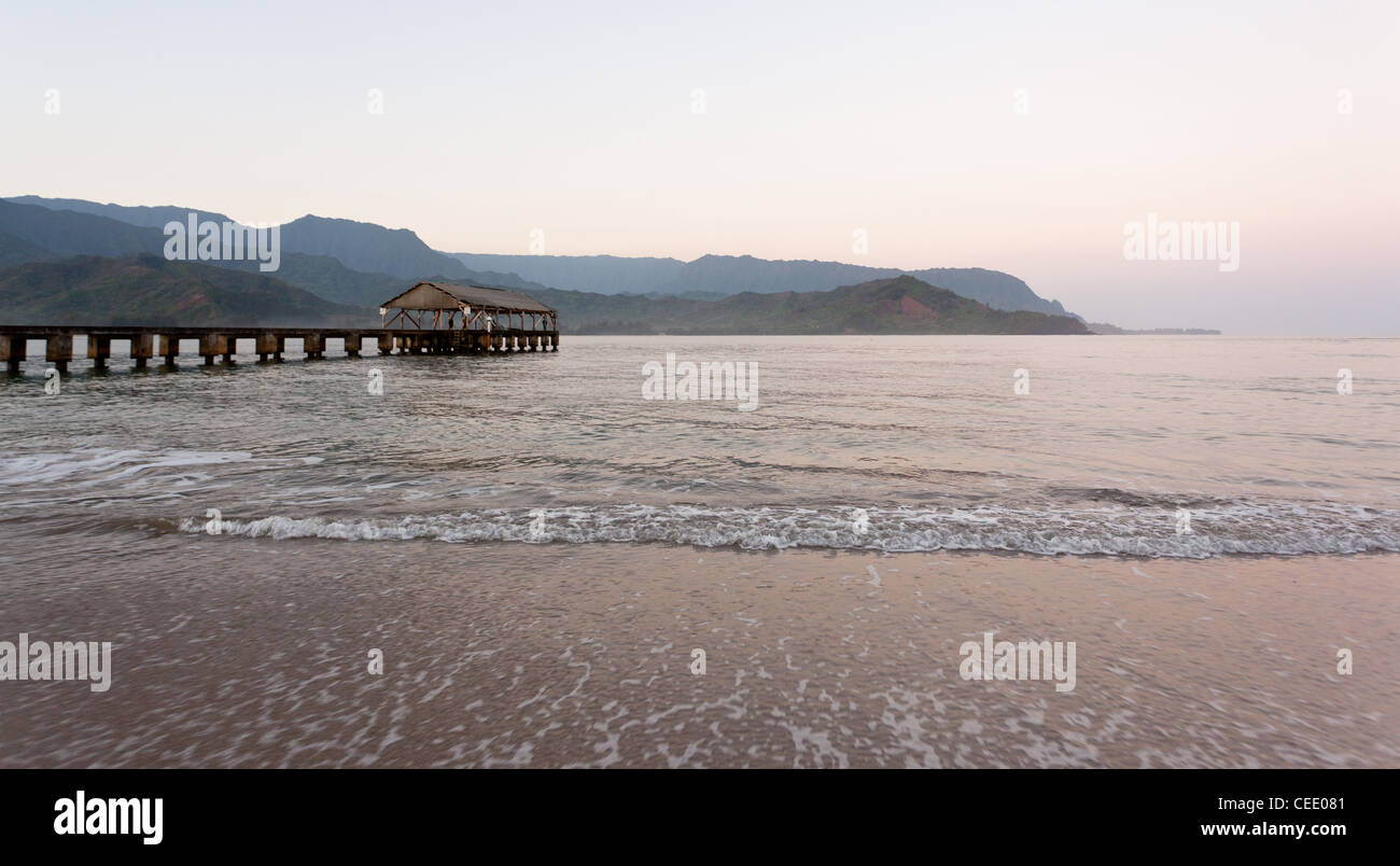 Aufgehende Sonne beleuchtet die Hanalei Pier und Na Pali Berge in Kauai Stockfoto